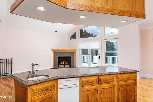 kitchen with lofted ceiling, sink, a tiled fireplace, a kitchen island with sink, and light hardwood / wood-style flooring