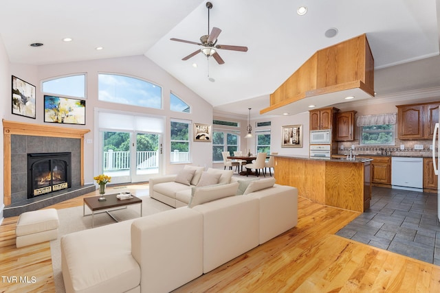 living room featuring a fireplace, high vaulted ceiling, sink, ceiling fan, and light wood-type flooring