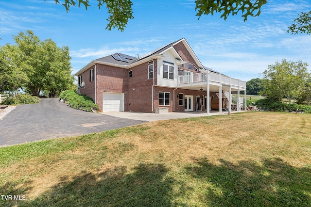 rear view of property with a patio, a deck, a garage, a yard, and solar panels