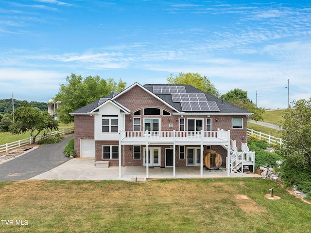 back of property featuring a garage, a yard, a patio area, and solar panels