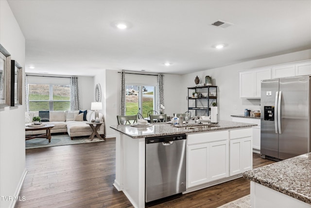 kitchen with light stone countertops, stainless steel appliances, white cabinets, and a kitchen island with sink