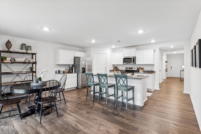 kitchen with a breakfast bar, white cabinetry, appliances with stainless steel finishes, and a center island with sink