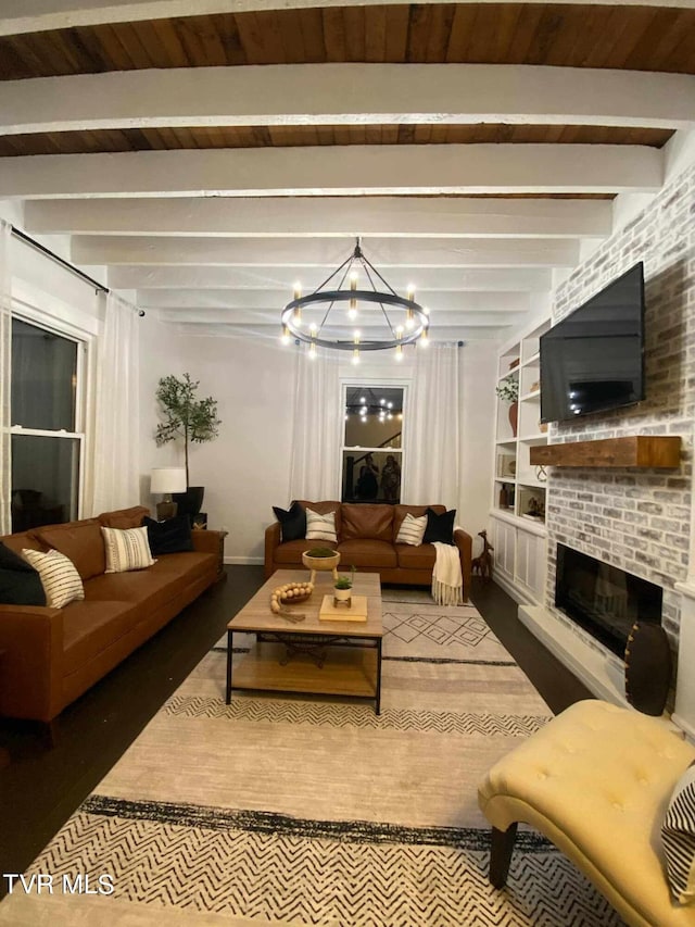 living room with a brick fireplace, built in features, beamed ceiling, and an inviting chandelier