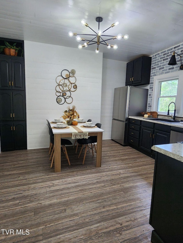 kitchen with a notable chandelier, dark hardwood / wood-style floors, sink, appliances with stainless steel finishes, and brick wall