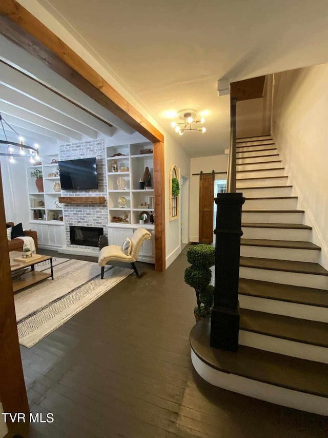 living room featuring wood-type flooring, built in features, vaulted ceiling, a brick fireplace, and a barn door