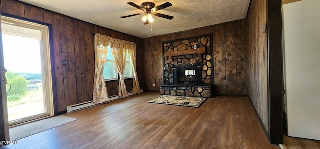 interior space with a baseboard heating unit, a stone fireplace, hardwood / wood-style floors, and wood walls