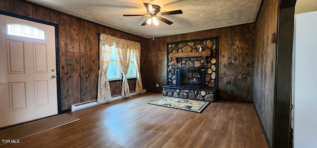 foyer entrance featuring ceiling fan, a baseboard heating unit, hardwood / wood-style floors, wooden walls, and a fireplace