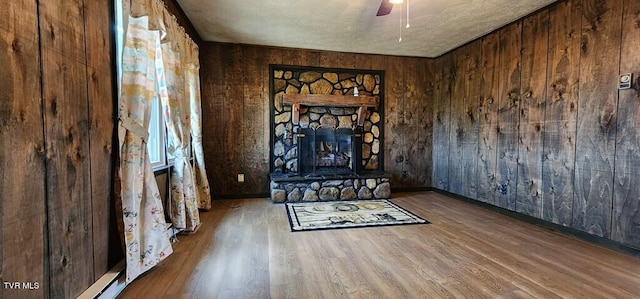 unfurnished living room with hardwood / wood-style floors, a fireplace, wooden walls, and ceiling fan