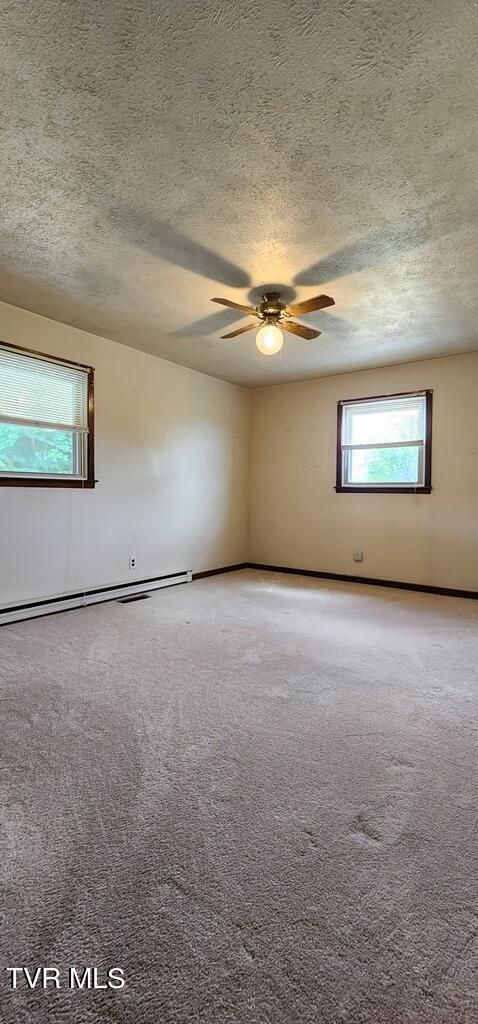 carpeted empty room with baseboard heating, ceiling fan, and a textured ceiling