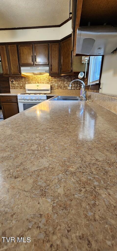 kitchen with sink, tasteful backsplash, dark brown cabinets, a textured ceiling, and white range with gas cooktop