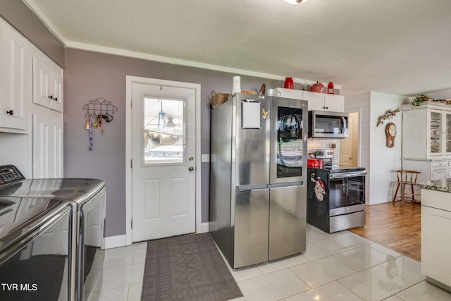 414 Beulah Church Dr, Kingsport, TN 37663 - kitchen with washing machine and clothes dryer, a textured ceiling, ornamental molding, stainless steel appliances, and white cabinetry