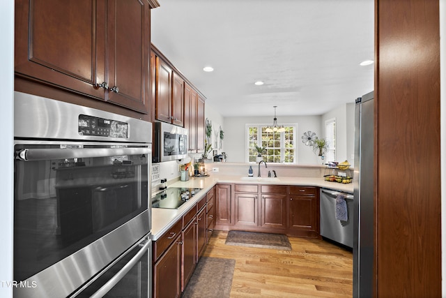 kitchen featuring decorative light fixtures, light hardwood / wood-style floors, stainless steel appliances, sink, and kitchen peninsula