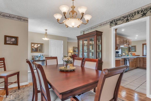 dining room featuring a textured ceiling, an inviting chandelier, sink, and light hardwood / wood-style floors