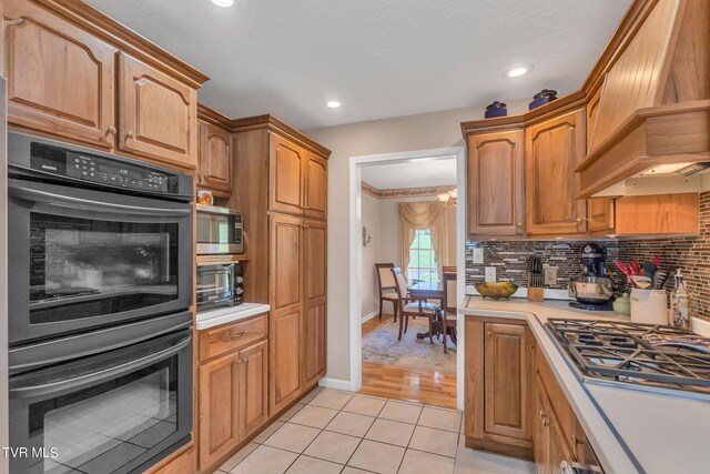 kitchen with stainless steel appliances, premium range hood, decorative backsplash, and light hardwood / wood-style floors