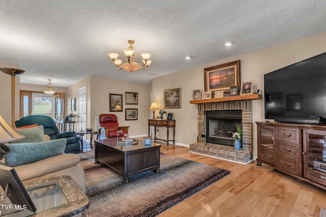 living room with a textured ceiling, an inviting chandelier, hardwood / wood-style floors, and a brick fireplace