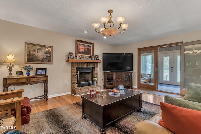 living room with a textured ceiling, a notable chandelier, a brick fireplace, and hardwood / wood-style flooring