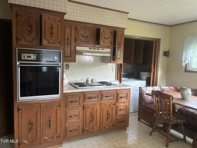 kitchen with washer / dryer, gas stovetop, crown molding, black oven, and backsplash