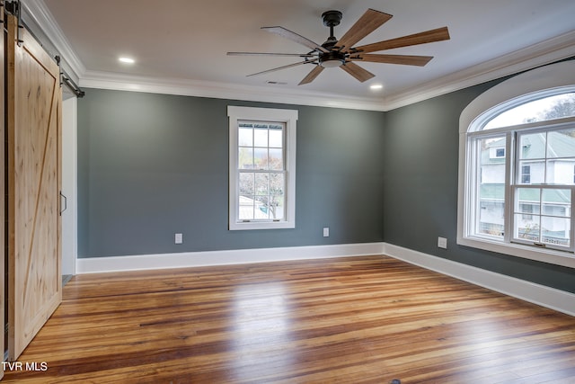 empty room with a barn door, hardwood / wood-style flooring, ceiling fan, and crown molding