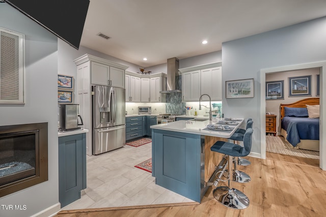 kitchen featuring a breakfast bar area, light hardwood / wood-style flooring, wall chimney range hood, stainless steel fridge, and sink