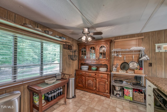 interior space with dishwashing machine, a textured ceiling, light tile patterned flooring, wood walls, and ceiling fan