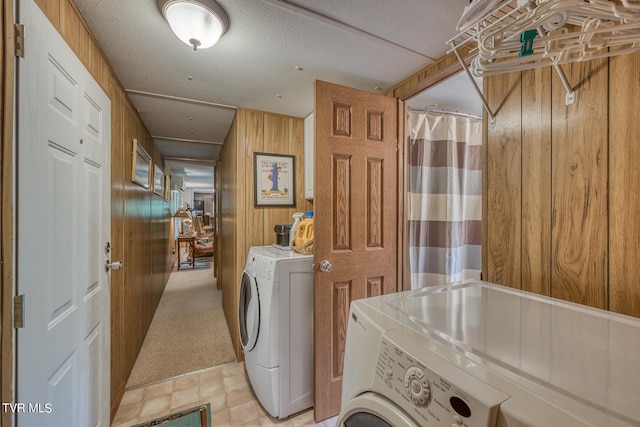 laundry area featuring light tile patterned flooring, wood walls, washer and dryer, and a textured ceiling