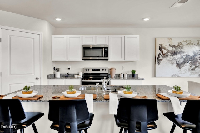 kitchen with dark stone countertops, appliances with stainless steel finishes, white cabinets, and a breakfast bar area