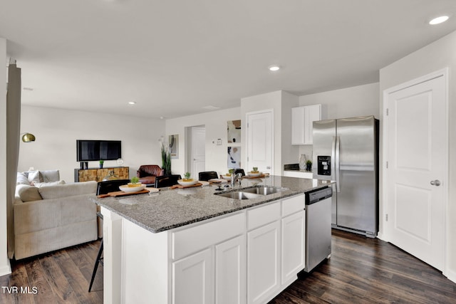 kitchen with white cabinetry, a kitchen island with sink, stainless steel appliances, sink, and dark stone counters