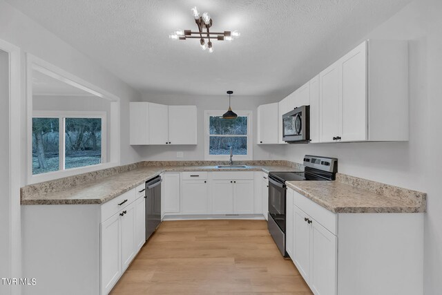 kitchen with decorative light fixtures, stainless steel appliances, white cabinets, light hardwood / wood-style flooring, and a textured ceiling