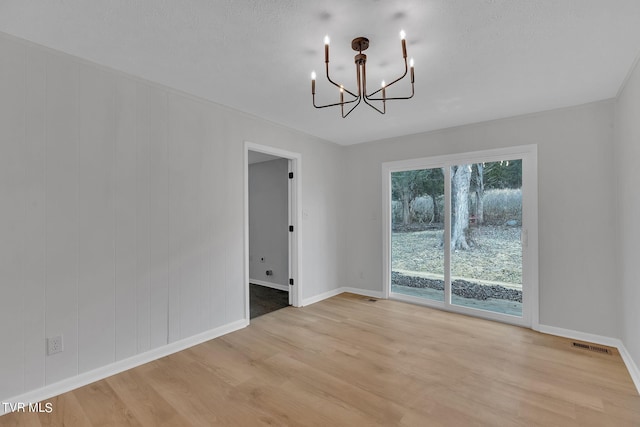 unfurnished room featuring an inviting chandelier and light hardwood / wood-style flooring