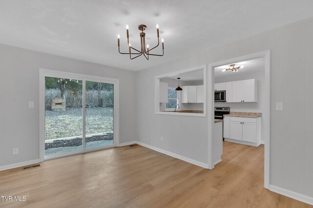 unfurnished dining area with sink, light hardwood / wood-style flooring, and a notable chandelier