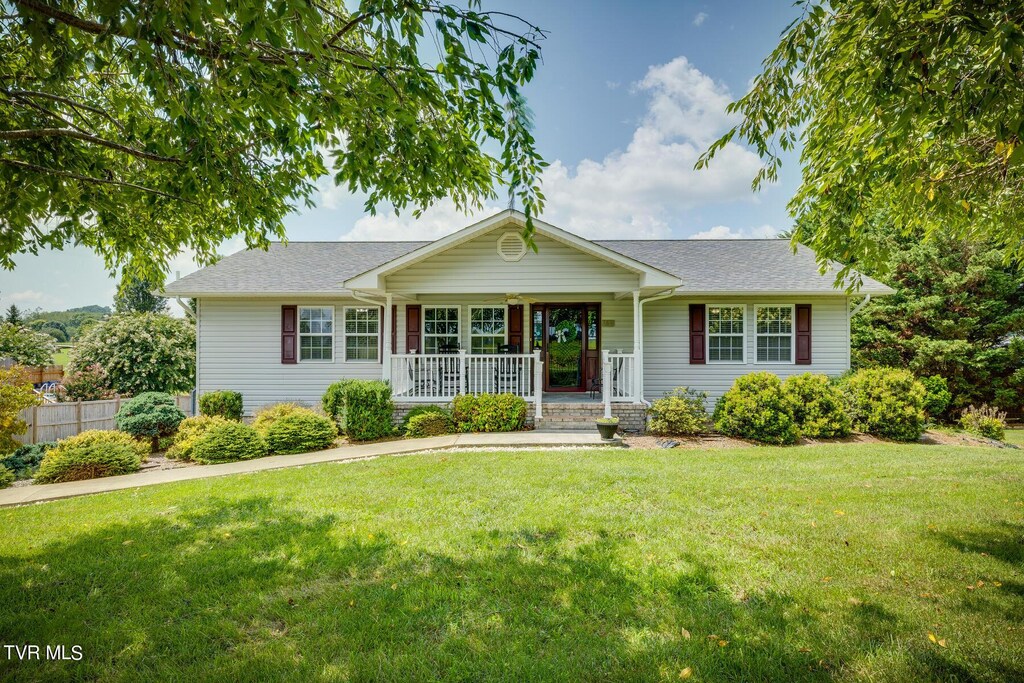 ranch-style home with a front yard, a porch, fence, and roof with shingles
