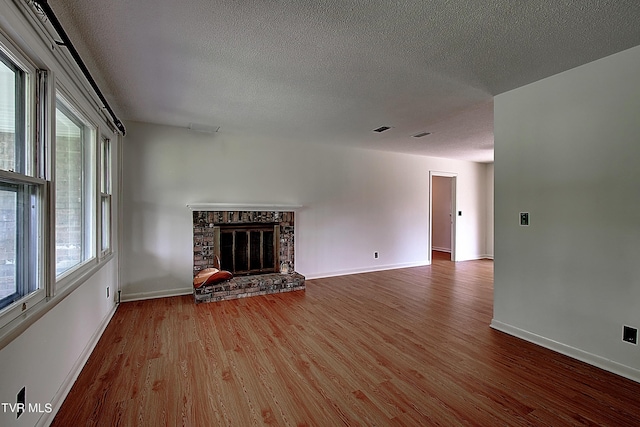 unfurnished living room featuring hardwood / wood-style flooring, a stone fireplace, and a textured ceiling