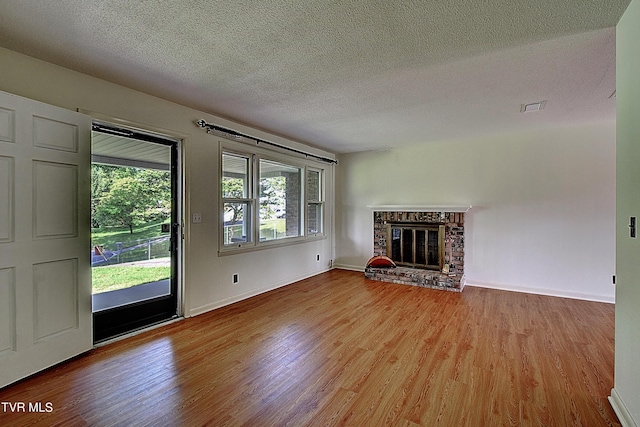 unfurnished living room with wood-type flooring, a brick fireplace, and a textured ceiling