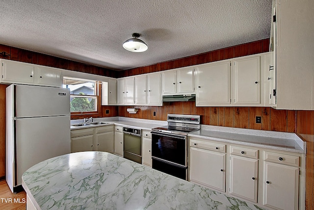 kitchen featuring a textured ceiling, wooden walls, stainless steel appliances, and white cabinets