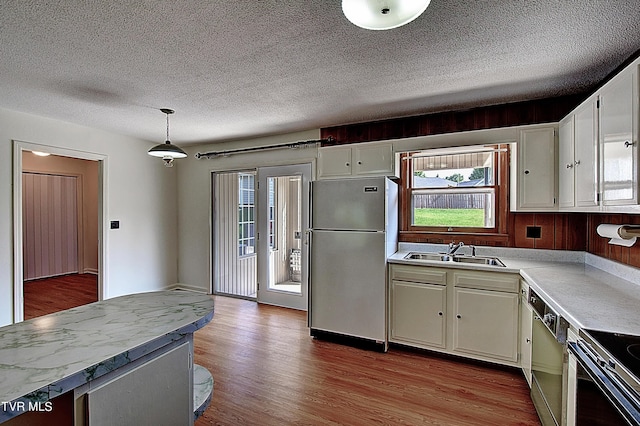 kitchen with stainless steel refrigerator, sink, dishwashing machine, hanging light fixtures, and light wood-type flooring