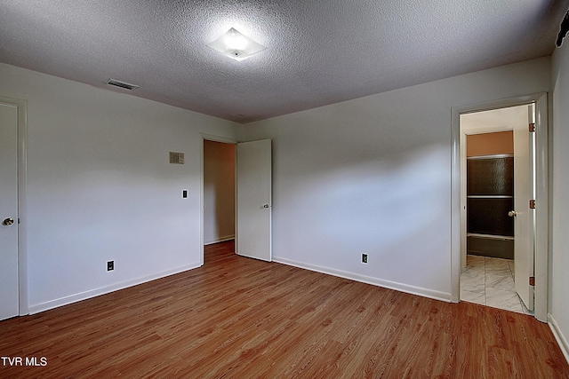 unfurnished bedroom featuring connected bathroom, a textured ceiling, and light wood-type flooring