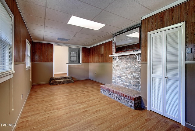 empty room with a paneled ceiling, wooden walls, and light hardwood / wood-style flooring