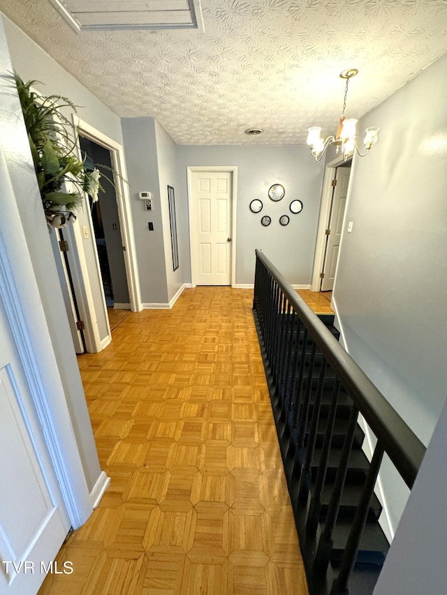 hallway featuring a notable chandelier, light parquet flooring, and a textured ceiling