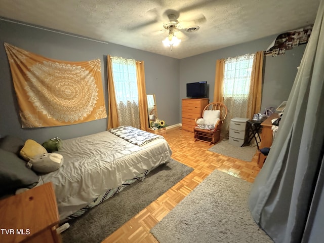 bedroom with ceiling fan, light parquet flooring, and a textured ceiling