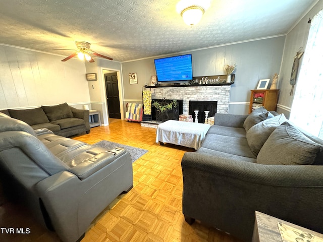 living room with a textured ceiling, ornamental molding, ceiling fan, a fireplace, and light parquet floors