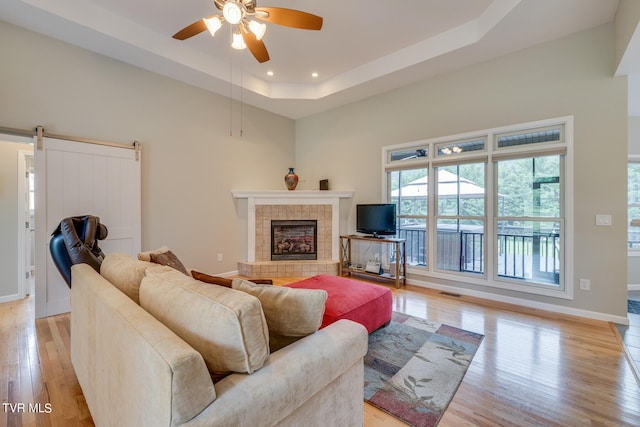 living room with light hardwood / wood-style floors, a raised ceiling, and ceiling fan