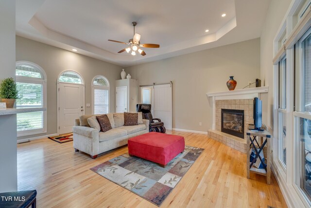 living room featuring light hardwood / wood-style floors, a fireplace, ceiling fan, and a raised ceiling