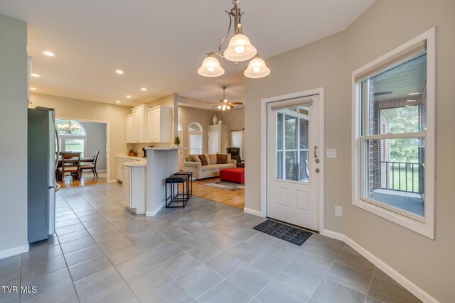 kitchen with light tile patterned flooring, white cabinets, a kitchen bar, stainless steel refrigerator, and kitchen peninsula