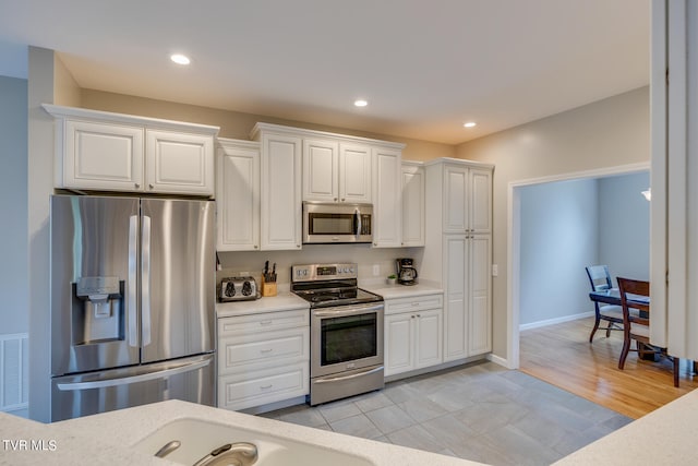 kitchen with stainless steel appliances, light hardwood / wood-style floors, and white cabinets