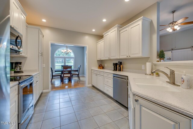 kitchen with sink, appliances with stainless steel finishes, ceiling fan with notable chandelier, and white cabinets