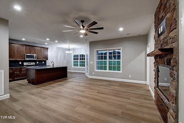 kitchen featuring ceiling fan with notable chandelier, a fireplace, a center island with sink, light hardwood / wood-style floors, and tasteful backsplash