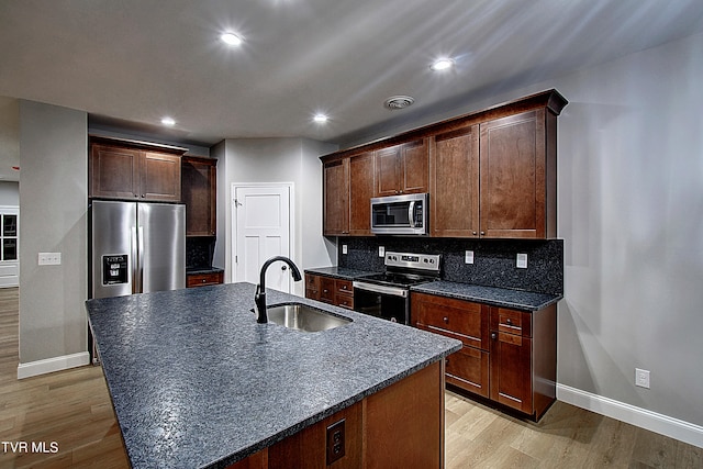 kitchen with appliances with stainless steel finishes, backsplash, sink, and light hardwood / wood-style flooring