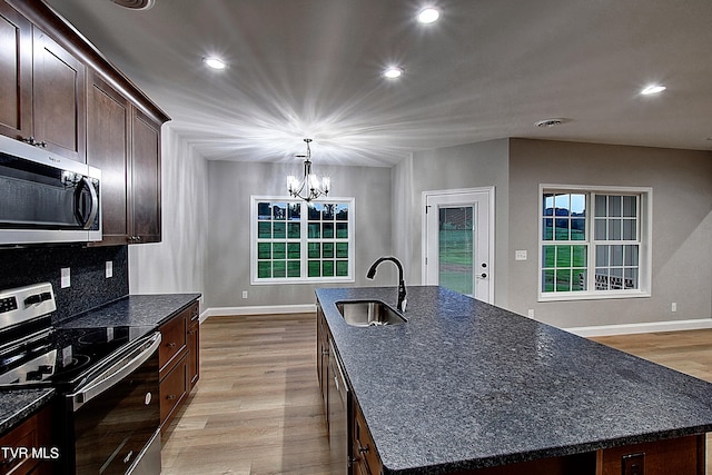 kitchen with light wood-type flooring, appliances with stainless steel finishes, a kitchen island with sink, sink, and decorative light fixtures