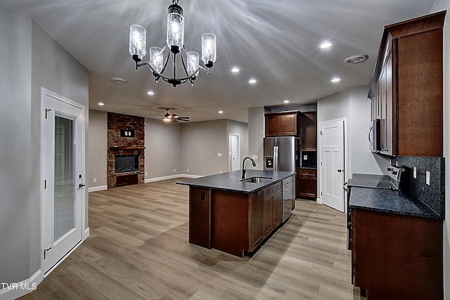 kitchen featuring light wood-type flooring, appliances with stainless steel finishes, a kitchen island with sink, sink, and decorative light fixtures