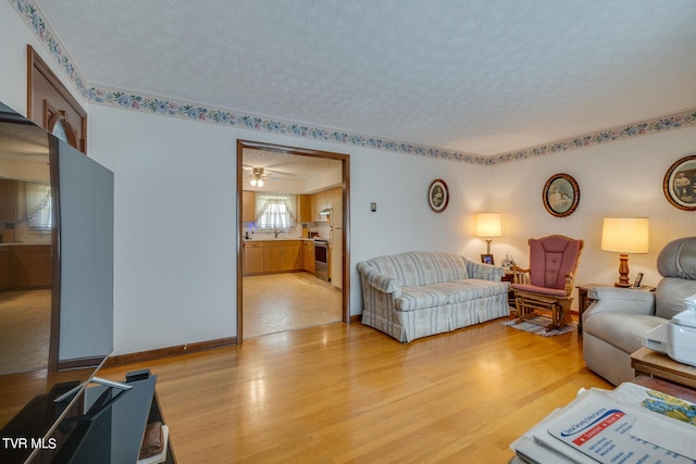 living room featuring ceiling fan, light hardwood / wood-style floors, and a textured ceiling